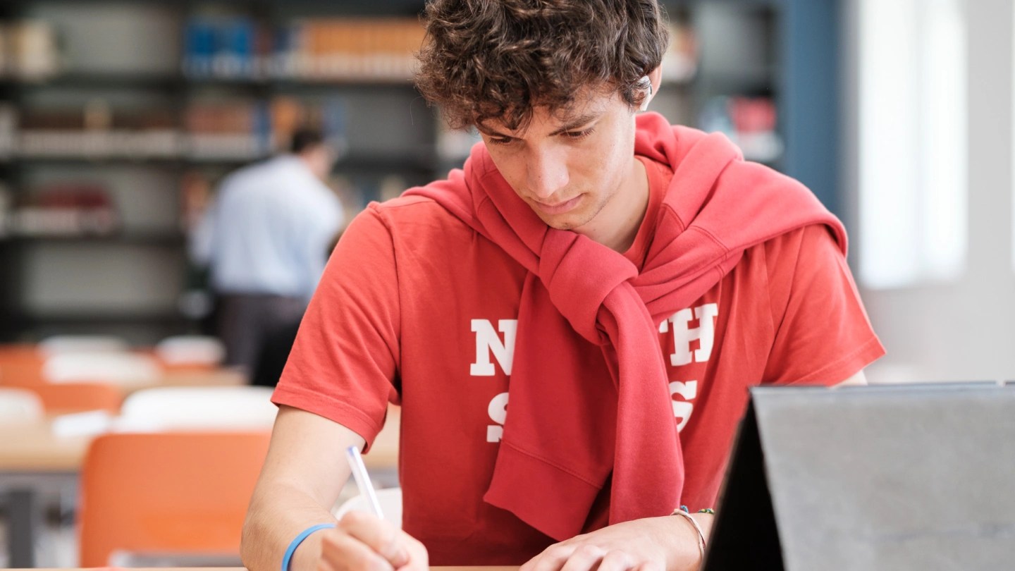 Ragazzo seduto in biblioteca che guarda in basso