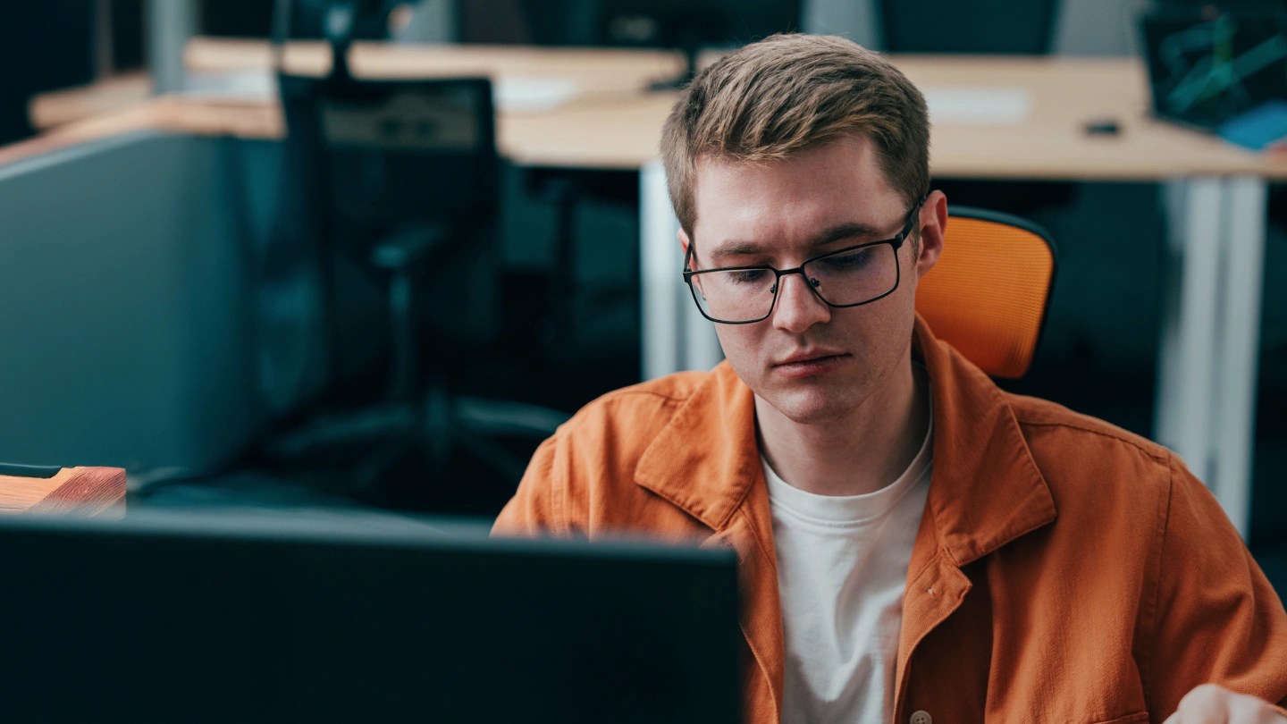 Uomo al computer in un ufficio con giacca arancione
