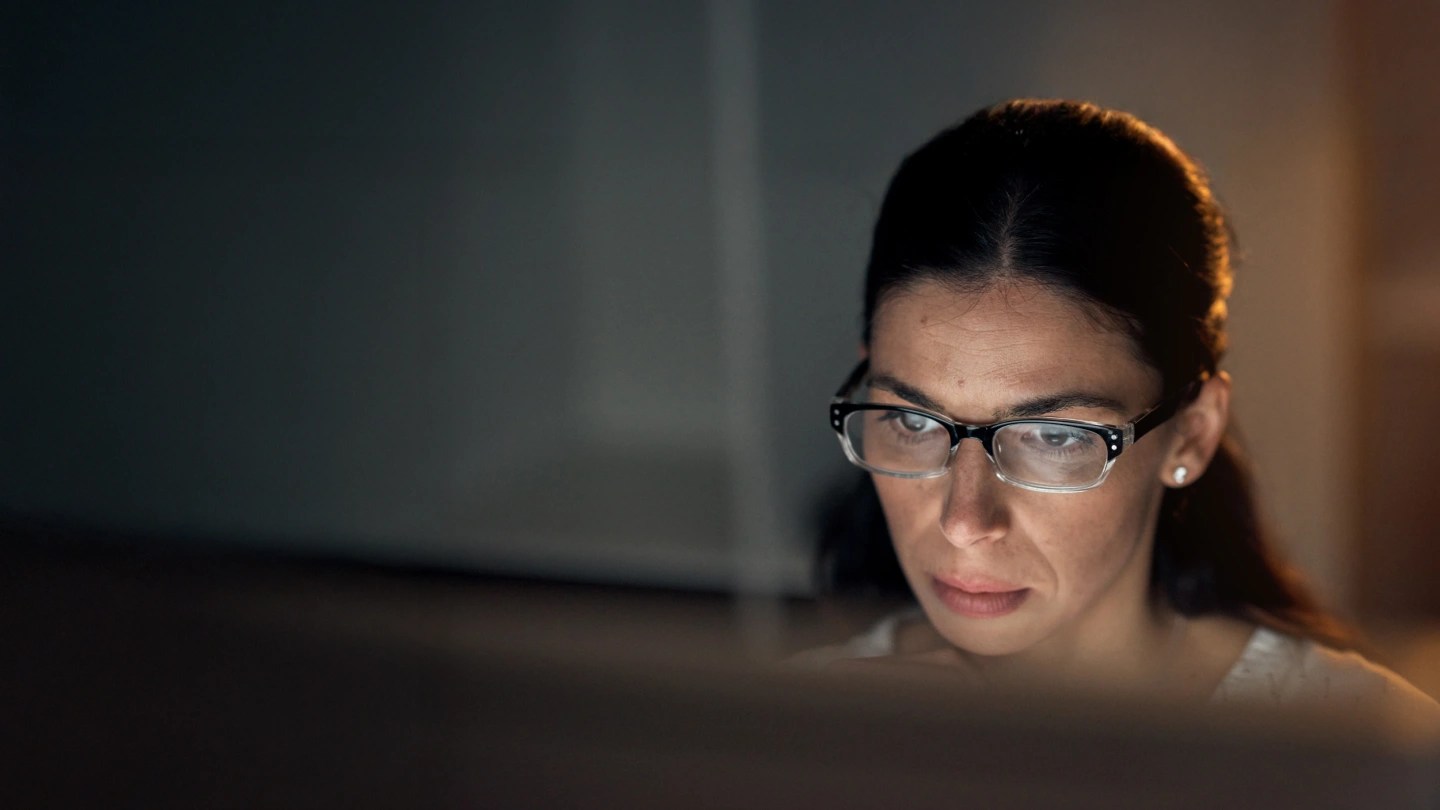 Donna con occhiali che lavora al computer in ambiente chiuso di sera