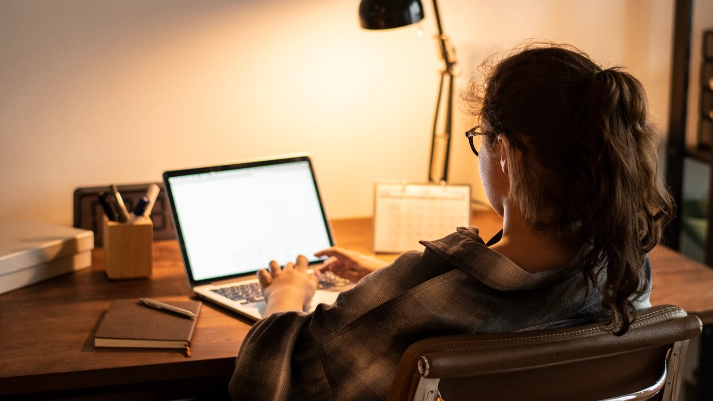 Ragazza di spalle che scrive al computer con luce da scrivania accesa