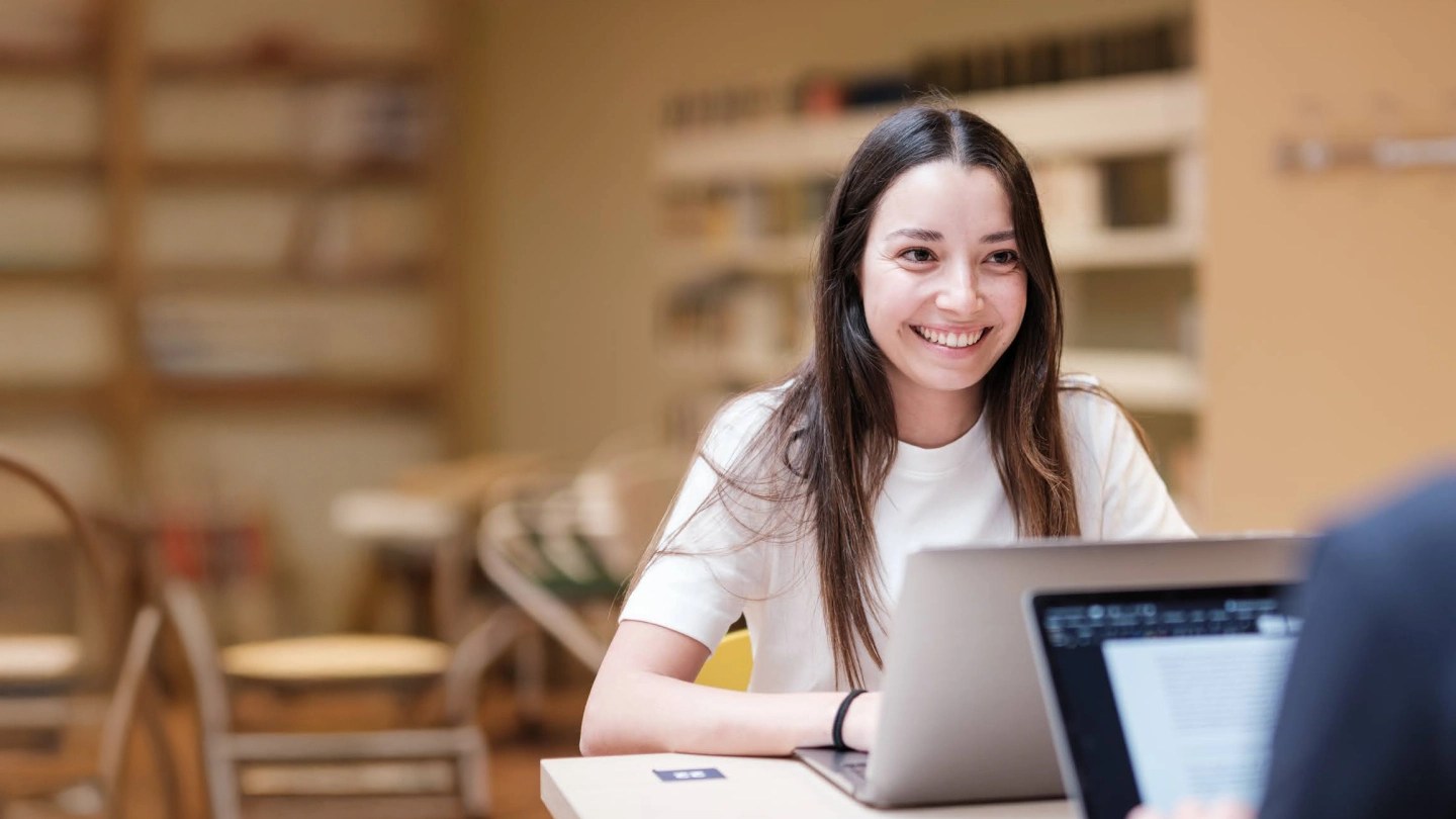 Ragazza al computer che sorride guardando qualcuno seduto di fronte a lei