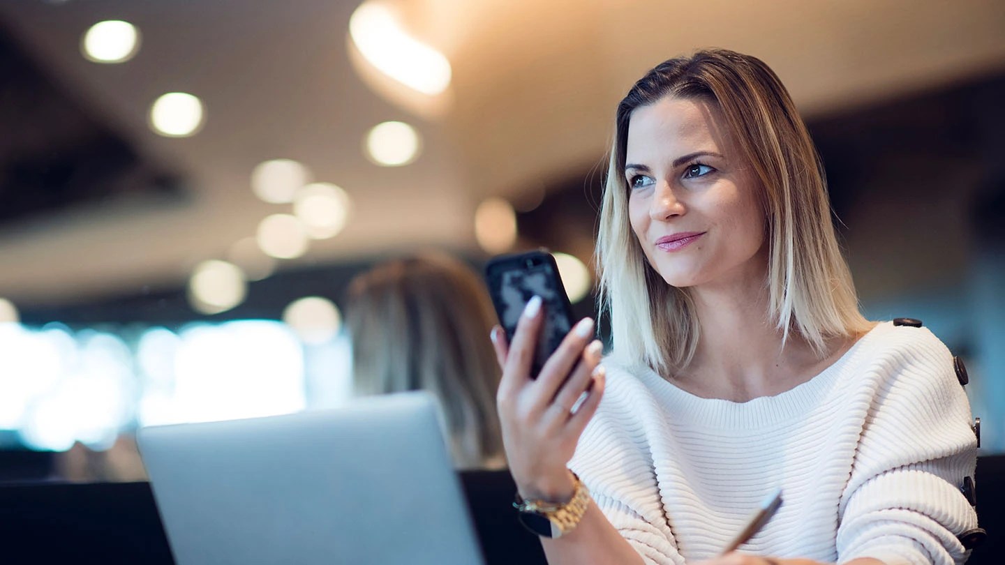 Donna davanti a un laptop con smartphone in mano