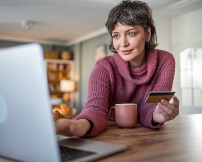 Ragazza a casa che fa un pagamento online davanti a un computer con una carta di credito tra le mani